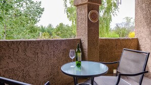 A glass table with a wine bottle and glass on it, a chair, and a view of greenery outside. - Signature 2 Bedroom Condo by RedAwning (Scottsdale)