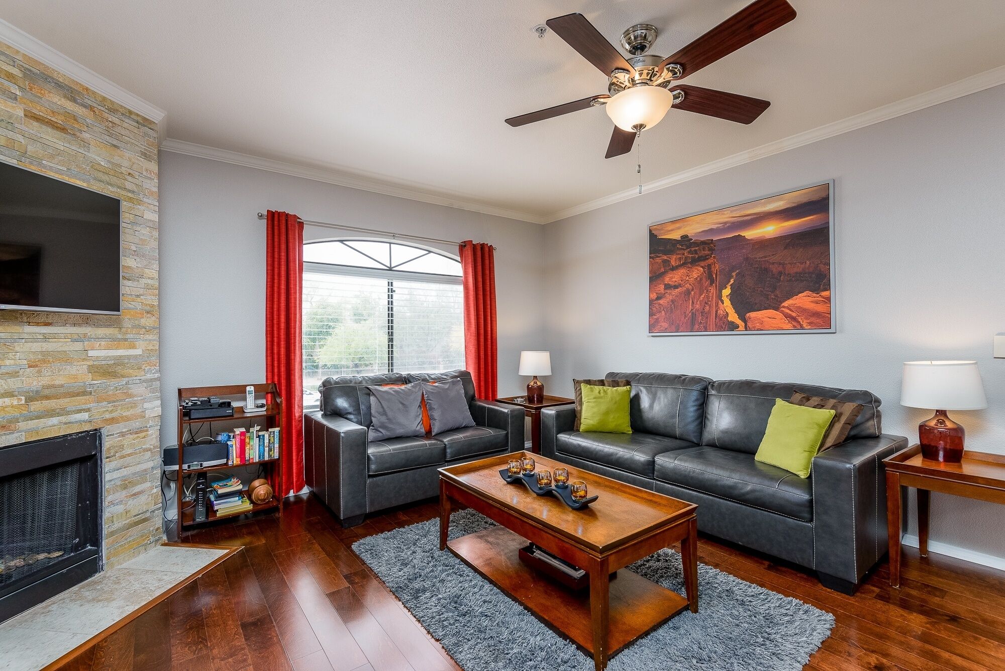 A living room with a fireplace, leather sofas, a coffee table, and a ceiling fan.
