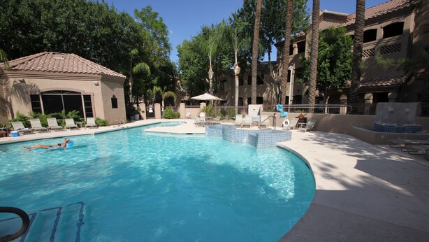 A swimming pool with lounge chairs and a covered area, surrounded by trees and buildings. - Signature 2 Bedroom Condo by RedAwning (Scottsdale)