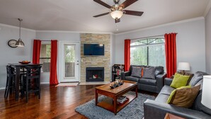 A living room with a fireplace, a ceiling fan, a dining area with a table and chairs, and a sofa with cushions. - Signature 2 Bedroom Condo by RedAwning (Scottsdale)