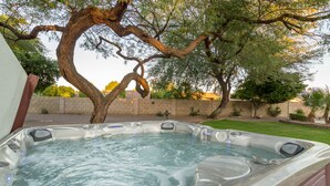 Un jacuzzi dans un jardin, avec un arbre et un mur de briques en arrière-plan.