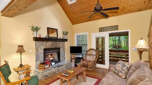 A cozy living room with a stone fireplace, a television, a rocking chair, and a sofa. - Hot Tub - Screen Porch - Rockers - Fire Pit - Cozy - Clean - Fast Wi-Fi - 5 Star (Maggie Valley)