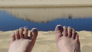 A pair of feet with blue-painted toenails resting on a sandy beach, with a calm body of water and a sandy dune in the background. - 500 m from the beach! Duplex, private wifi Fibre, bed linen, swimming pool, parking, benefits (Moliets-Et-Maa)