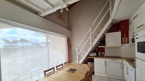 A modern kitchen with white cabinets, a wooden dining table, and a view of the outdoors through large windows. - 500 m from the beach! Duplex, private wifi Fibre, bed linen, swimming pool, parking, benefits (Moliets-Et-Maa)