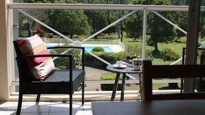 A room with a view of a pool and greenery, a wicker chair with a cushion, and a small table with a cup and saucer. - 500 m from the beach! Duplex, private wifi Fibre, bed linen, swimming pool, parking, benefits (Moliets-Et-Maa)