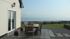 A patio with a table and chairs, a door, and a view of the sea. - Stunning Beachfront Cottage  Ballybunion (Ballybunion,)