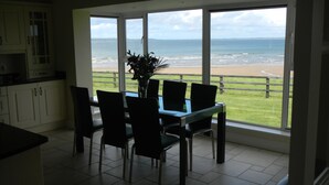 A dining area with a table and chairs, large windows with a view of the beach and ocean. - Stunning Beachfront Cottage  Ballybunion (Ballybunion,)
