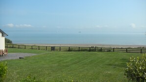 A grassy lawn with a wooden fence, a building with a sloped roof, and a view of the sea. - Stunning Beachfront Cottage  Ballybunion (Ballybunion,)