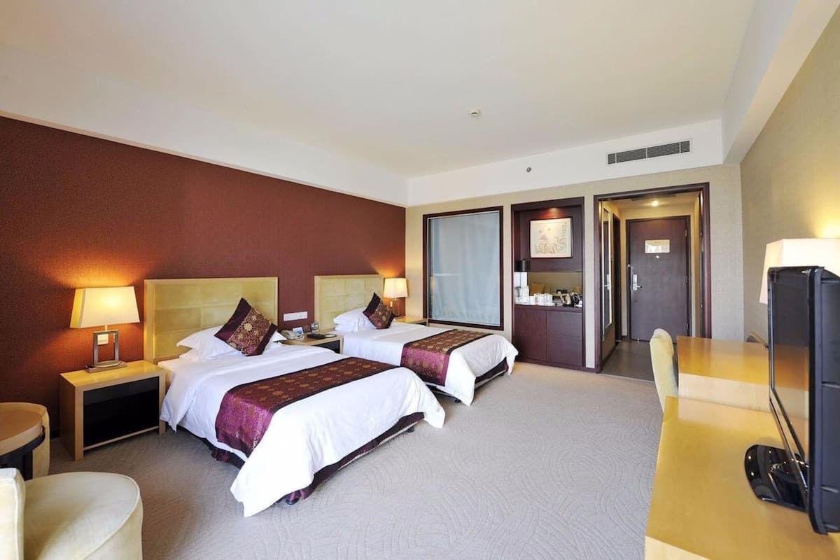 A hotel room with two beds, a desk, a chair, a TV, and a bathroom visible through an open door.