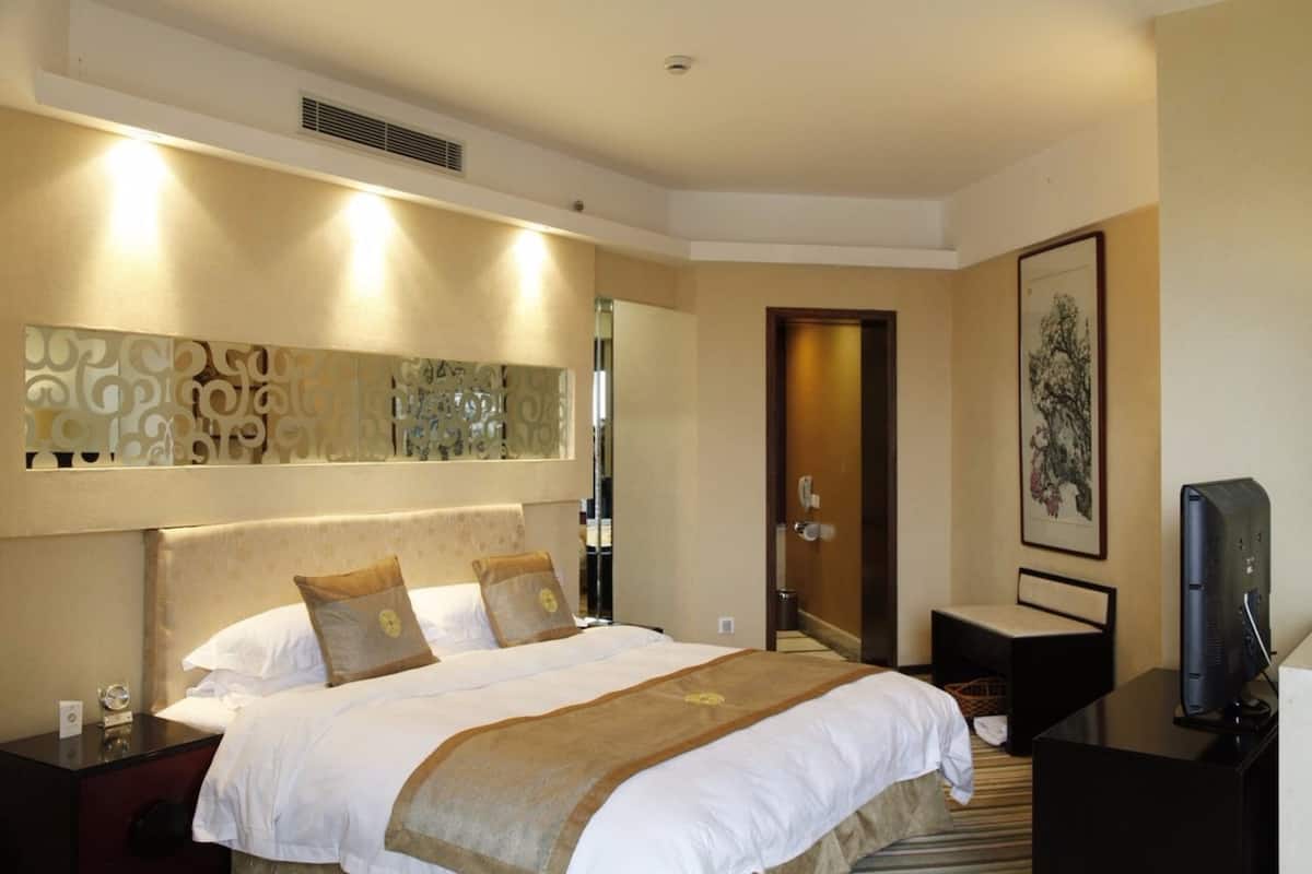 A hotel room with a large bed, a desk with a computer, a television, and a decorative wall piece.