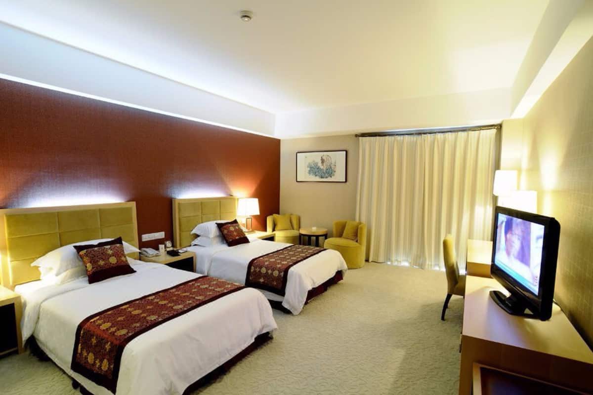 A hotel room with two beds, a television, a desk, a chair, a small table, and a window with curtains.