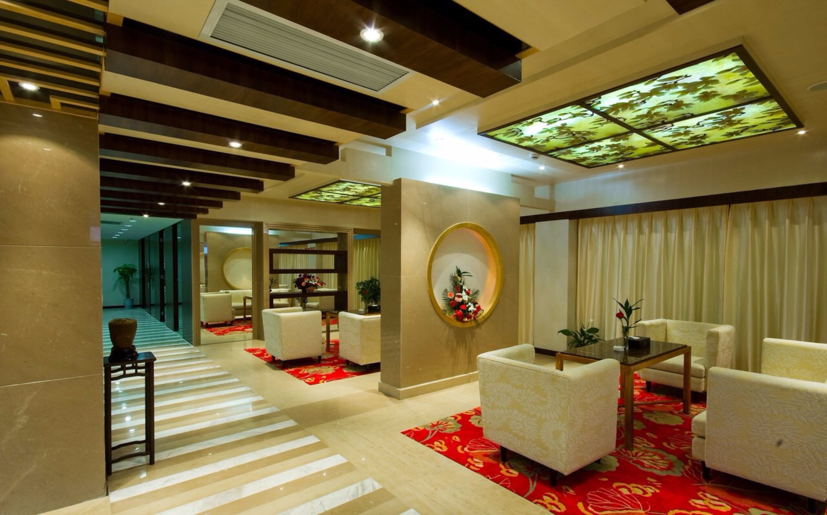 Un lobby moderno de hotel con un área de estar central, una recepción y una pared decorativa con un arreglo floral.