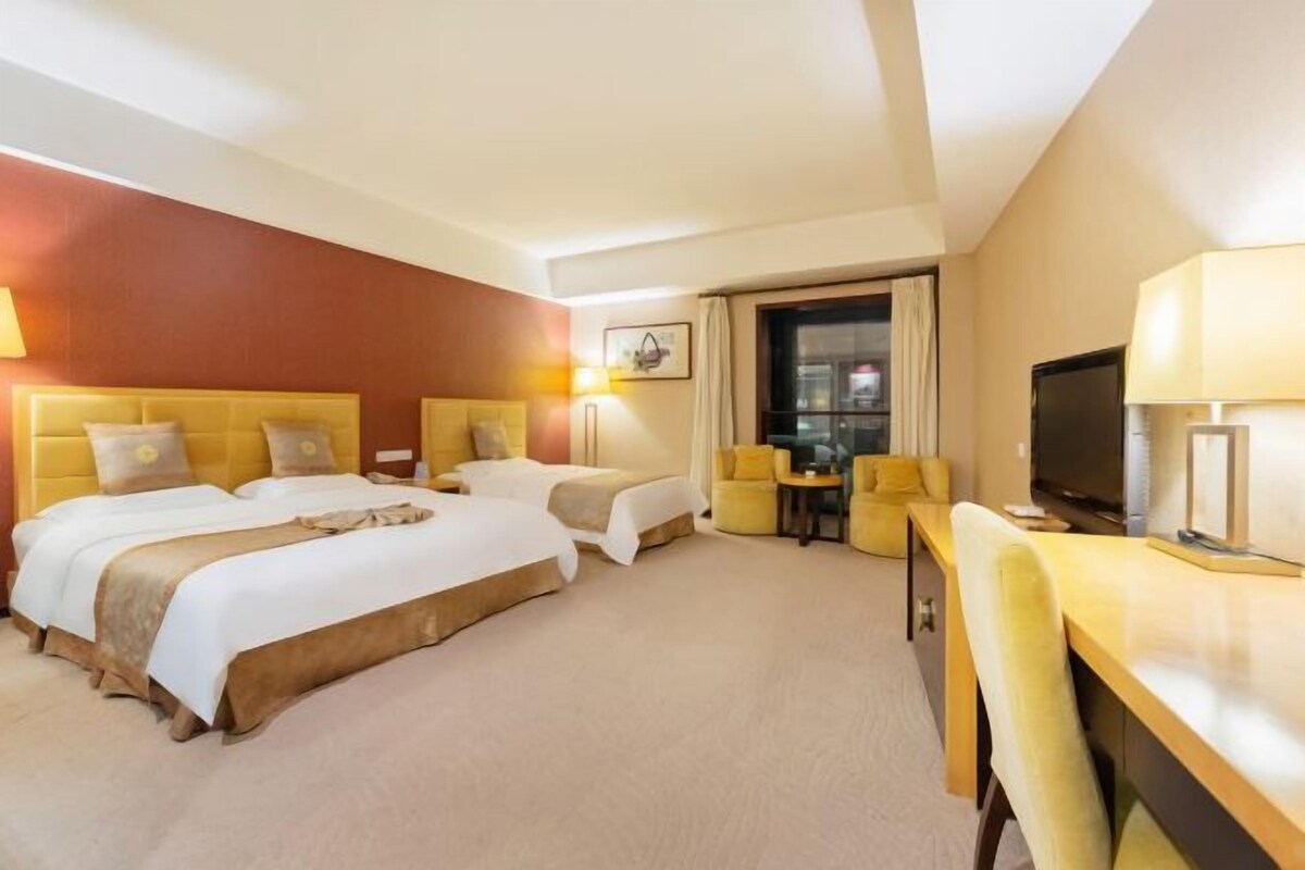 A hotel room with two beds, a desk, a chair, a television, and a window with curtains.