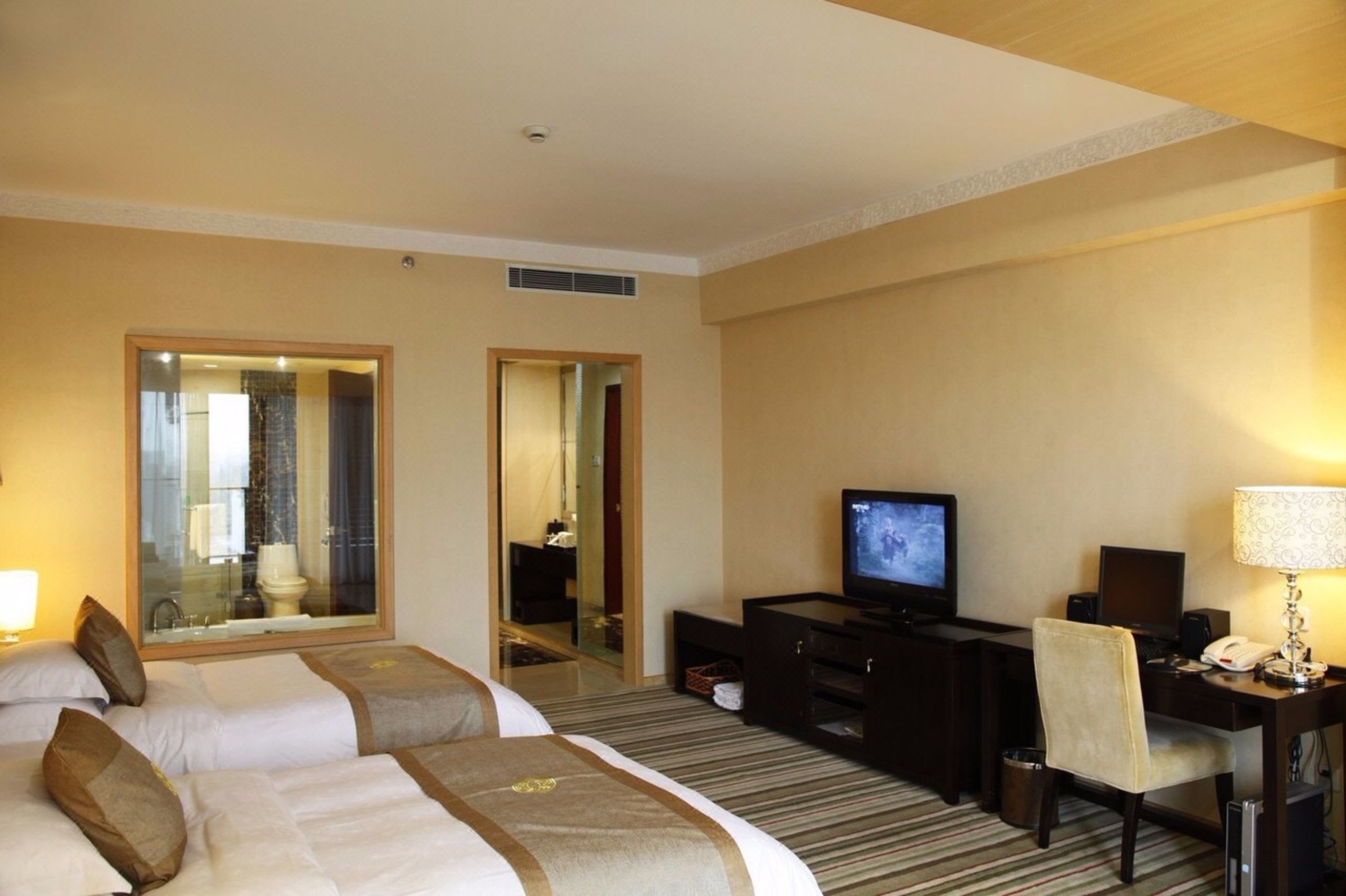 A hotel room with two beds, a television, a desk with a computer, and a mirror.