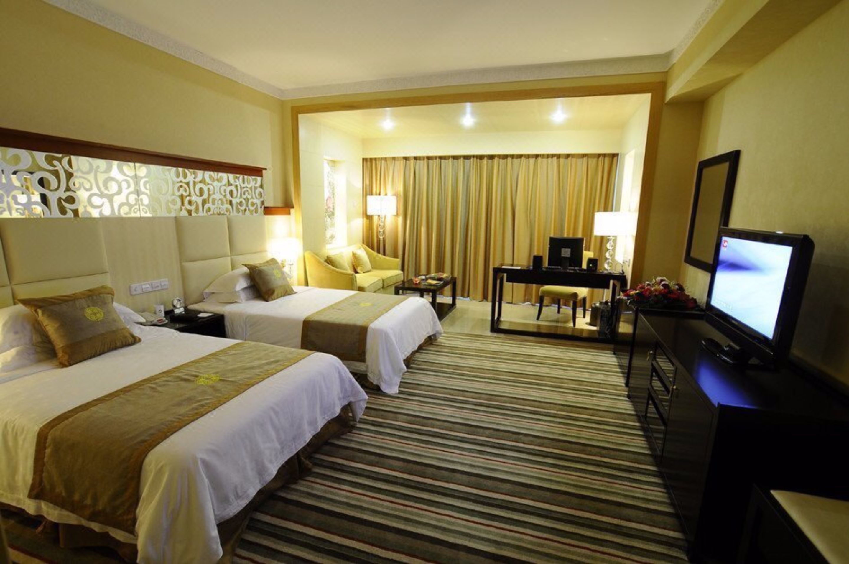 A hotel room with two beds, a desk, a television, and a mirror.
