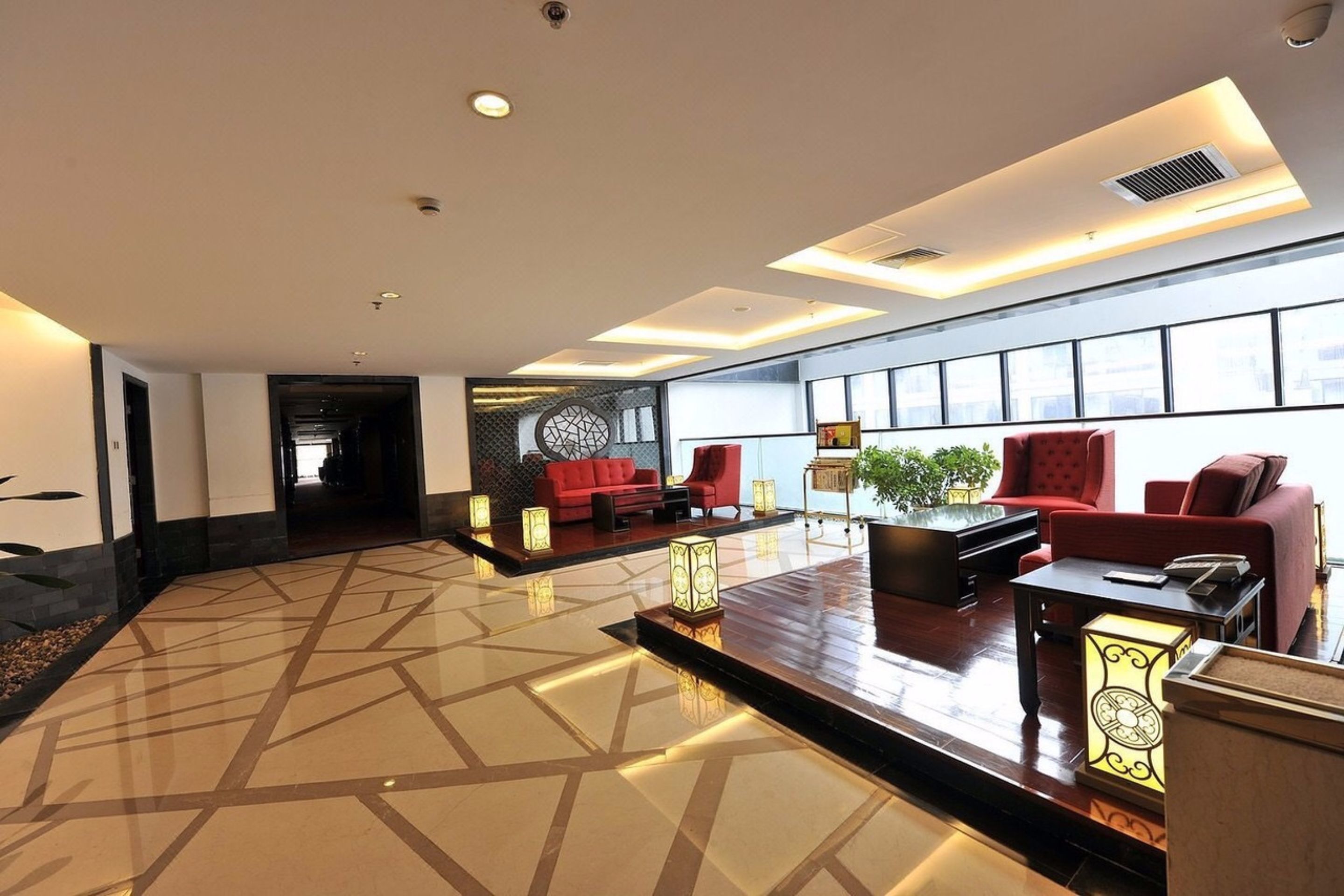 A spacious lobby with a geometric patterned floor, red sofas, a piano, and a large window offering a view of the city.