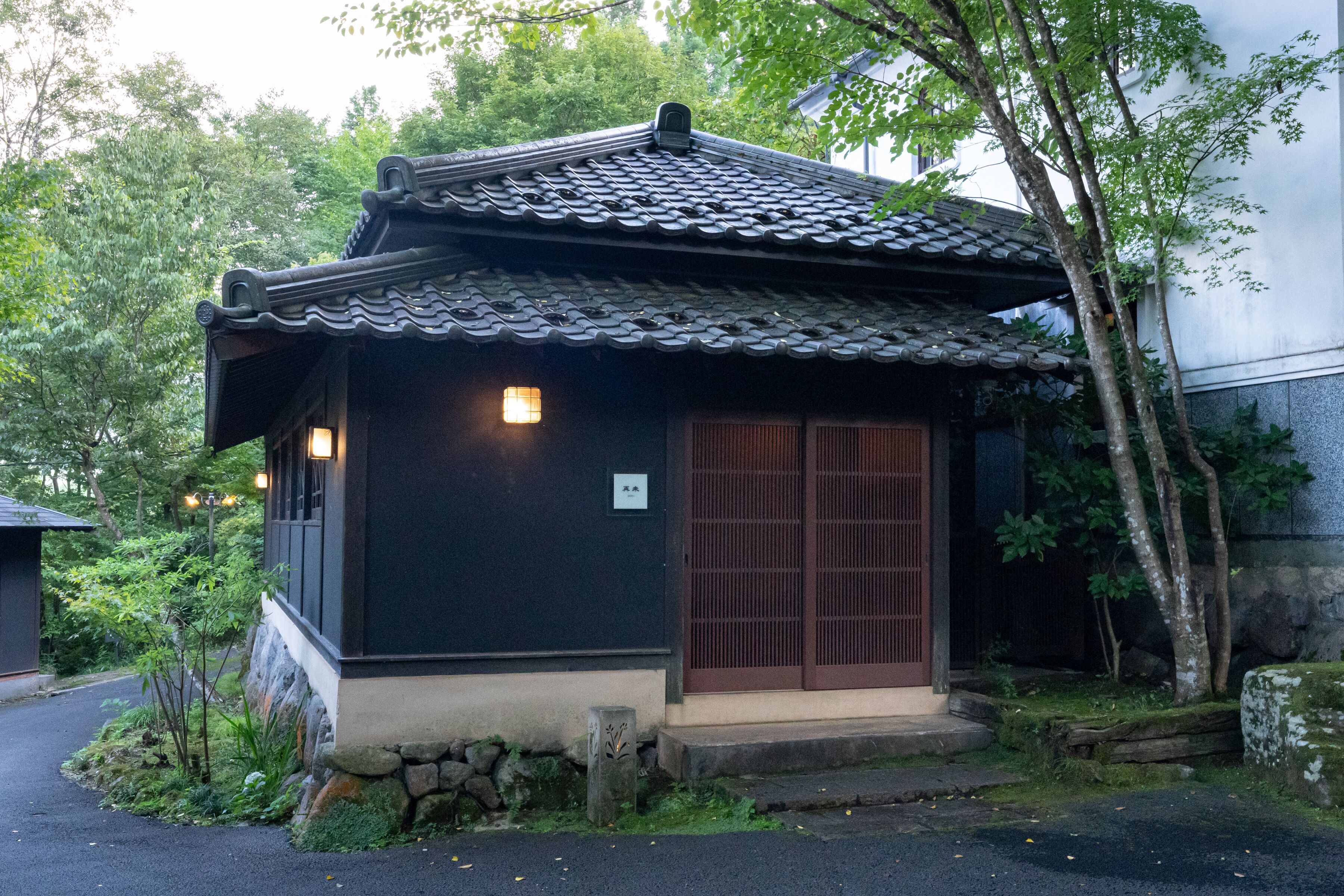 A traditional Japanese building with a tiled roof, a wooden door, and a small stone base.