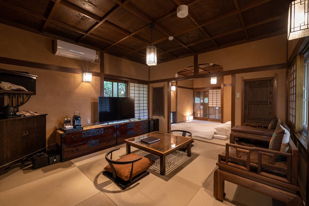 A traditional Japanese-style room with tatami flooring, a low wooden table, a sofa, and a television.