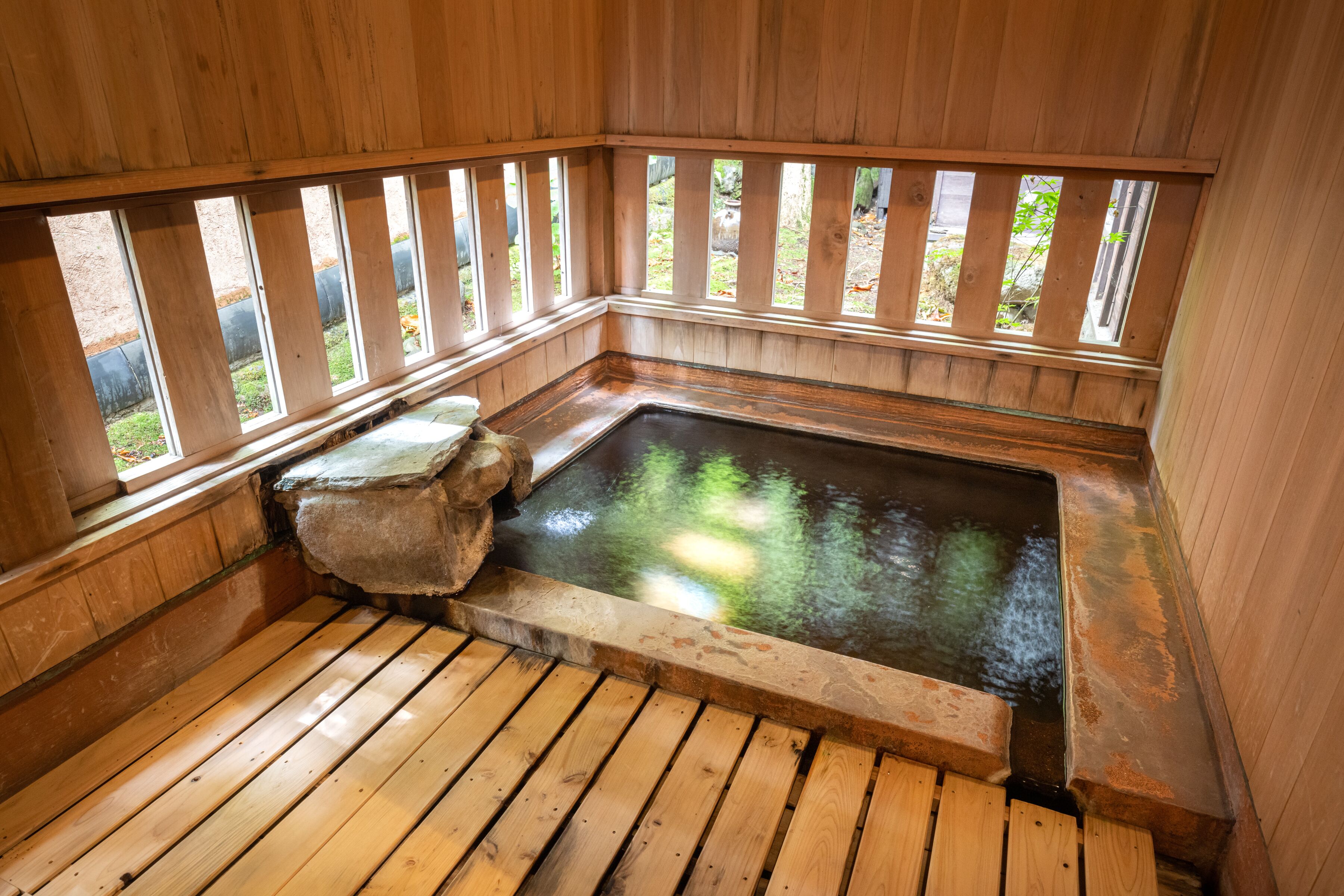 A wooden hot tub with a stone edge and a wooden deck.