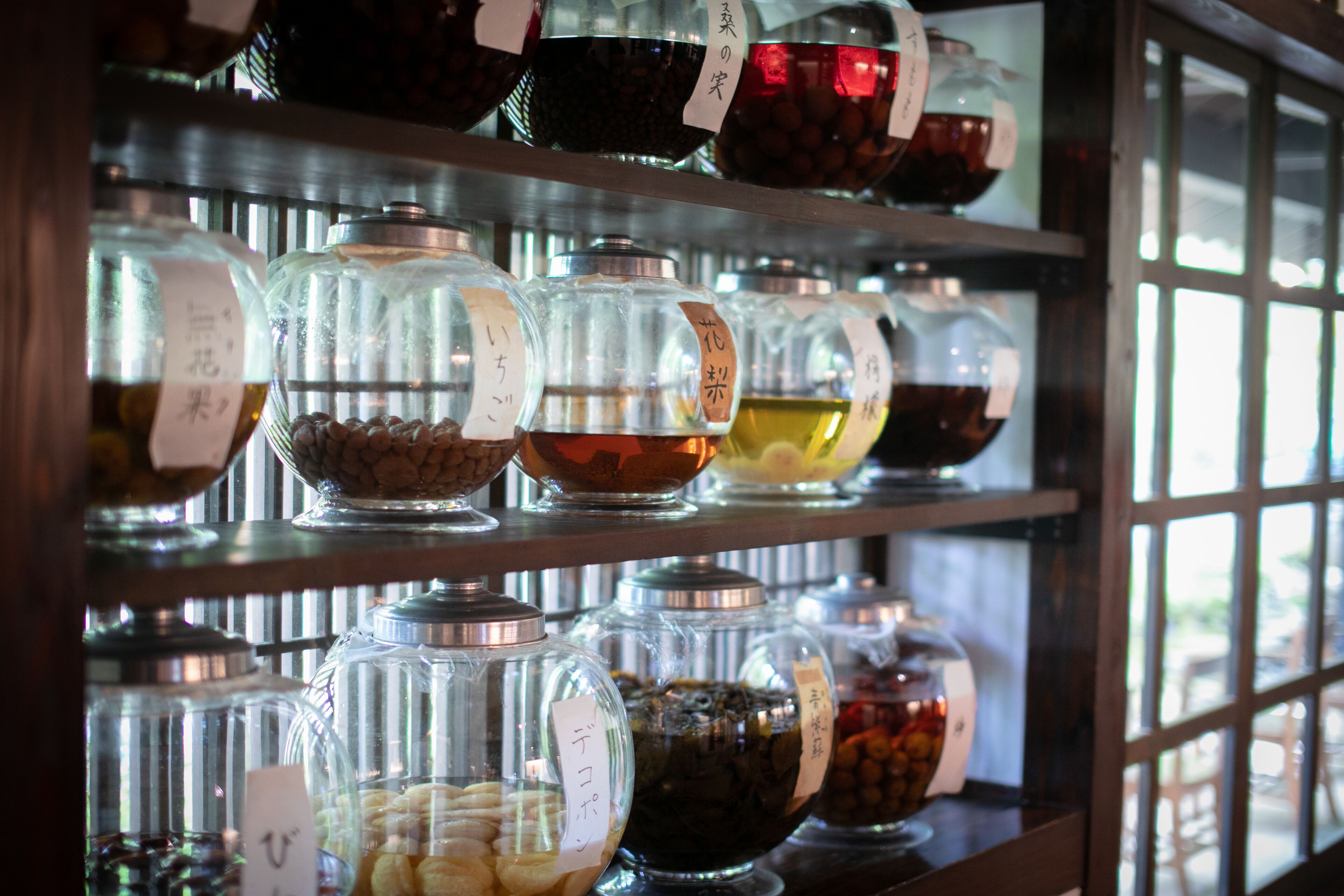 Une variété d’aliments sont présentés dans des récipients en verre, chacun étant muni d’une étiquette, et l’ensemble est disposé sur des étagères.
