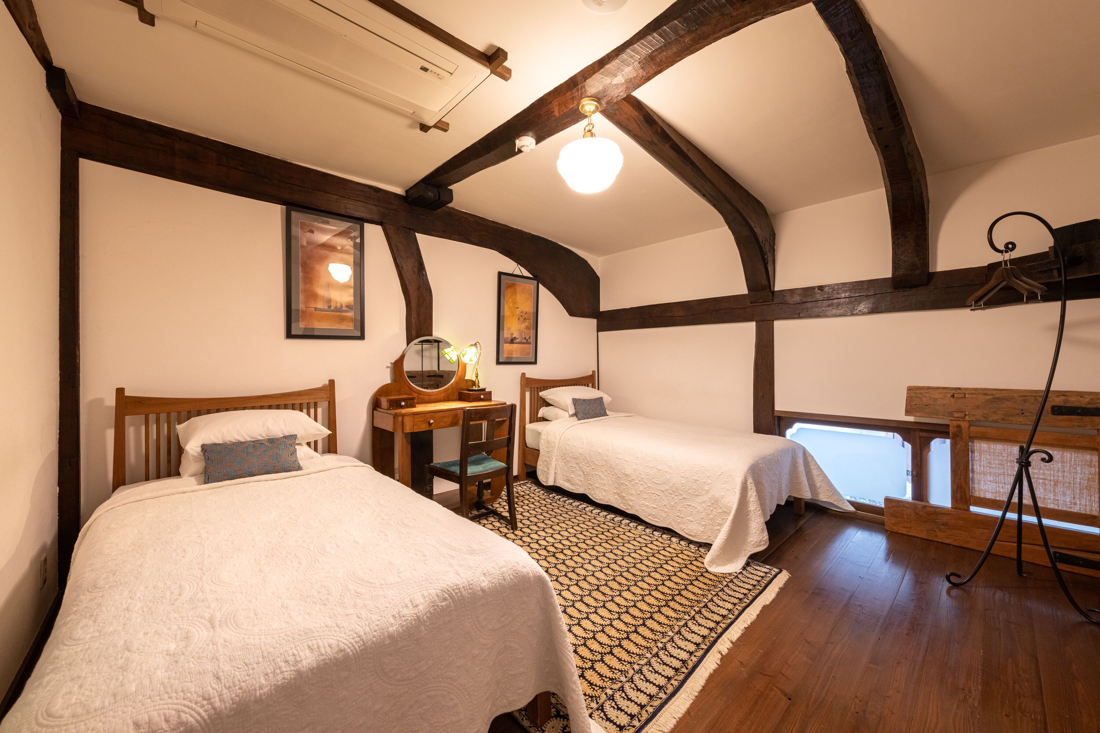 A bedroom with two beds, a wooden desk, and a large window.