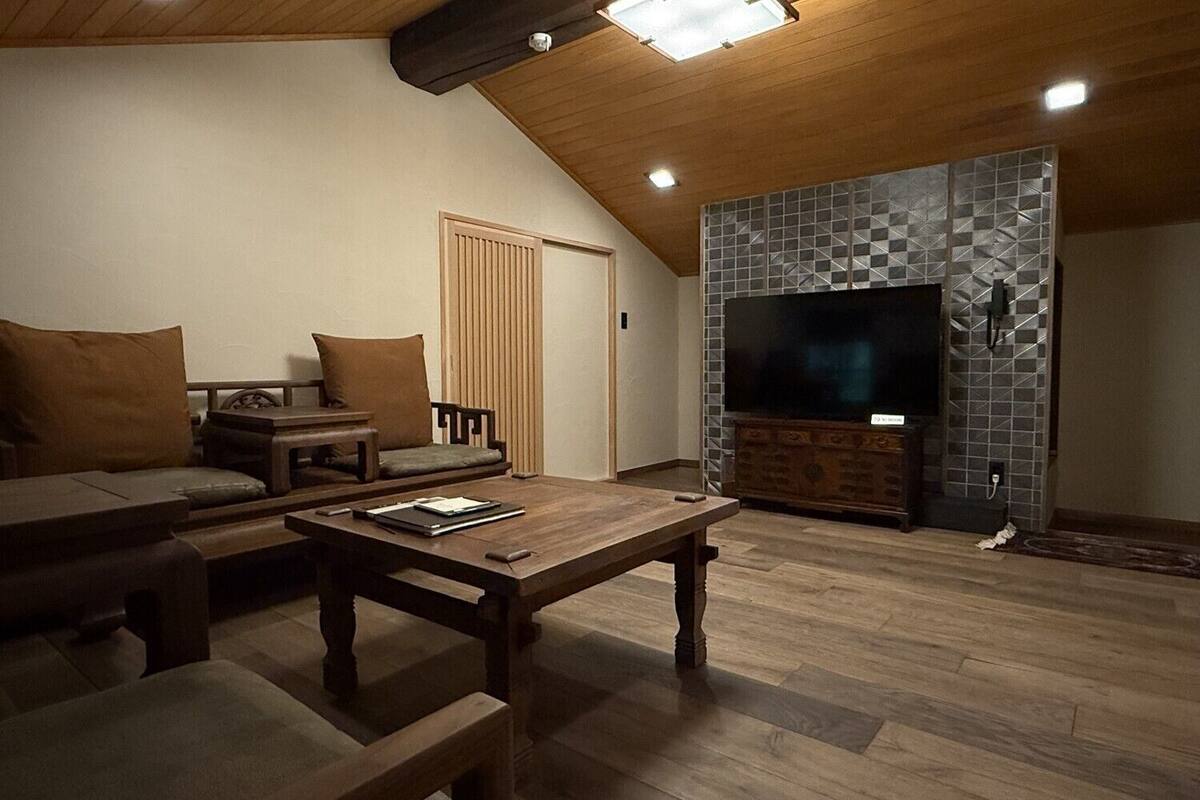 A cozy living room with a wooden ceiling, a large flat-screen TV, and a fireplace with a geometric tile design.