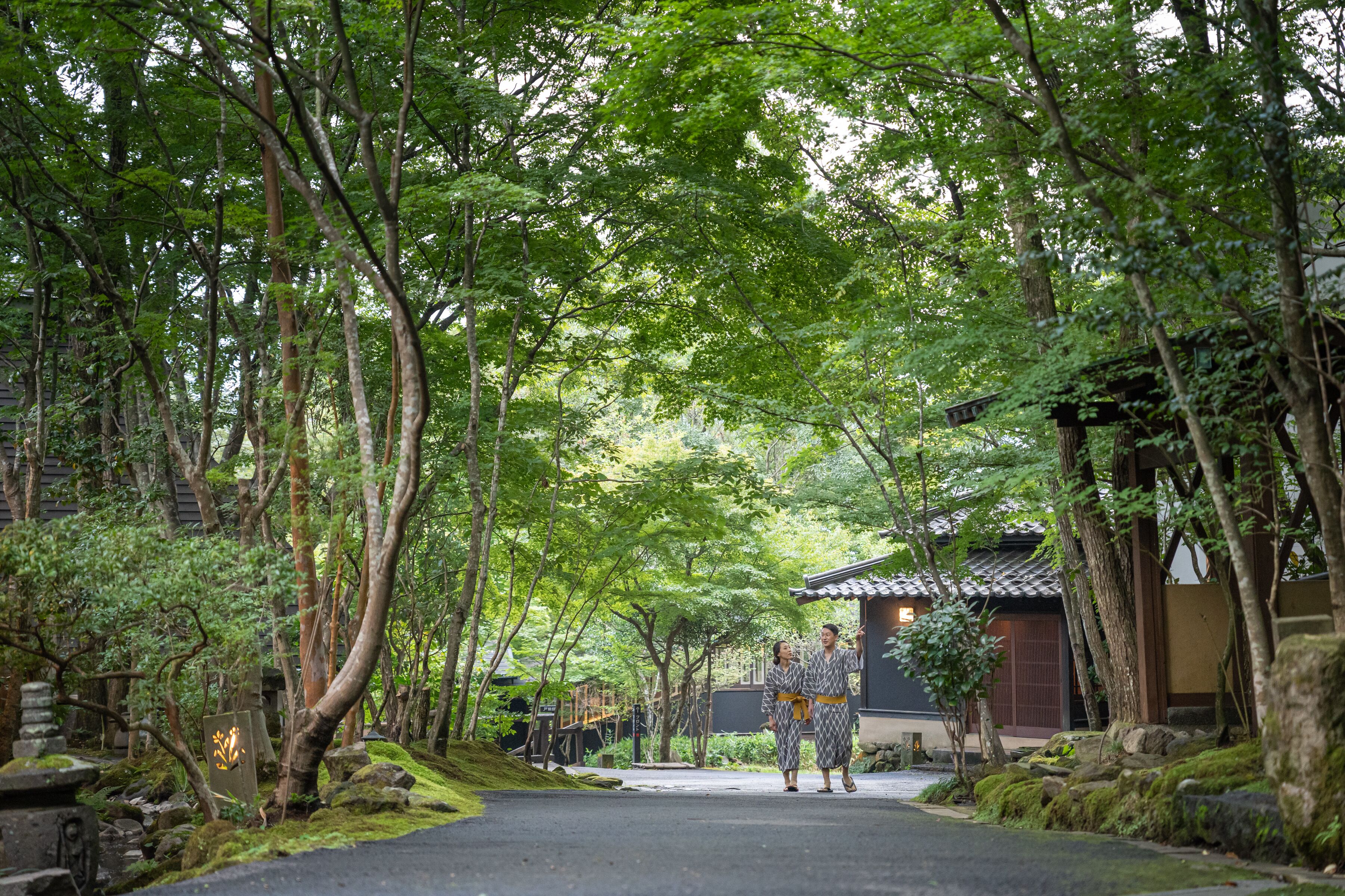 A traditional Japanese garden with a pathway, stone lanterns, and a building with a tiled roof.