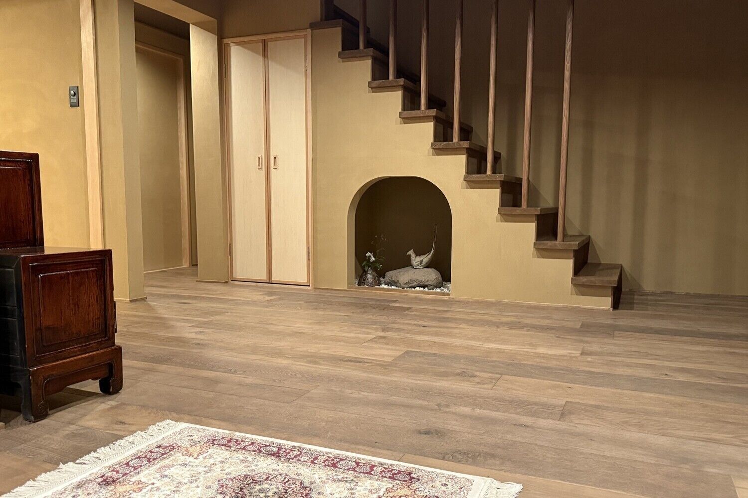 A spacious living room with a wooden staircase, a large wooden cabinet, and a decorative rug.