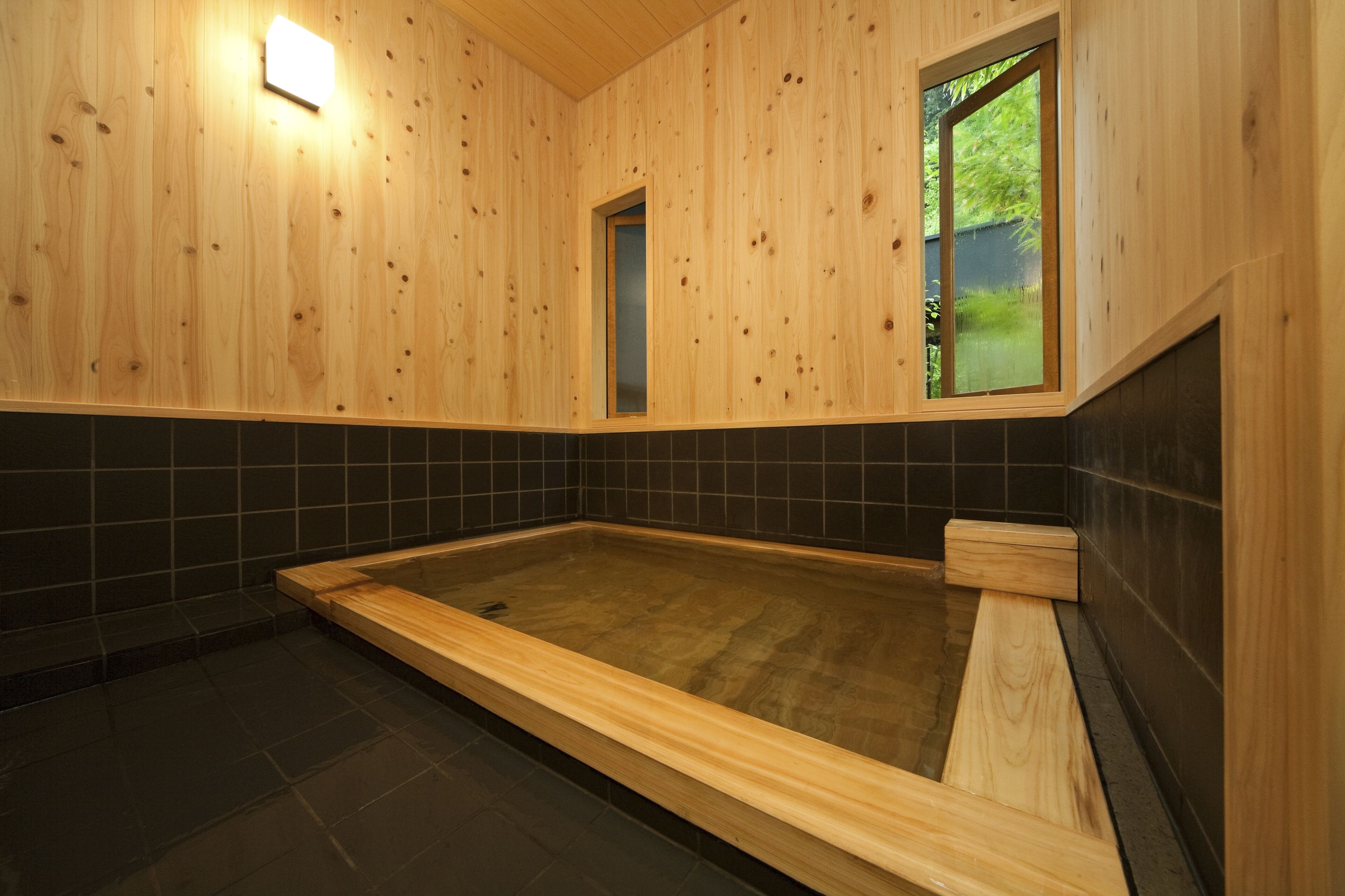 A wooden interior with a large wooden bathtub, a small window, and a tiled wall.