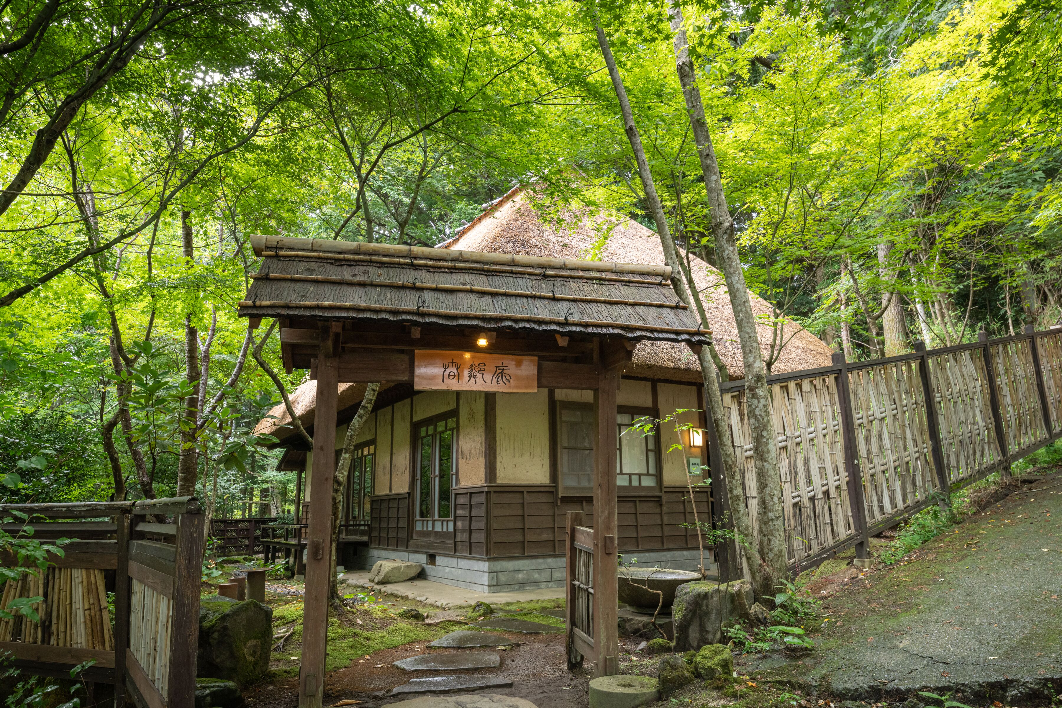 A traditional wooden structure with a thatched roof, surrounded by lush greenery and a wooden fence.
