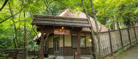 A traditional wooden structure with a thatched roof, surrounded by lush greenery and a wooden fence.