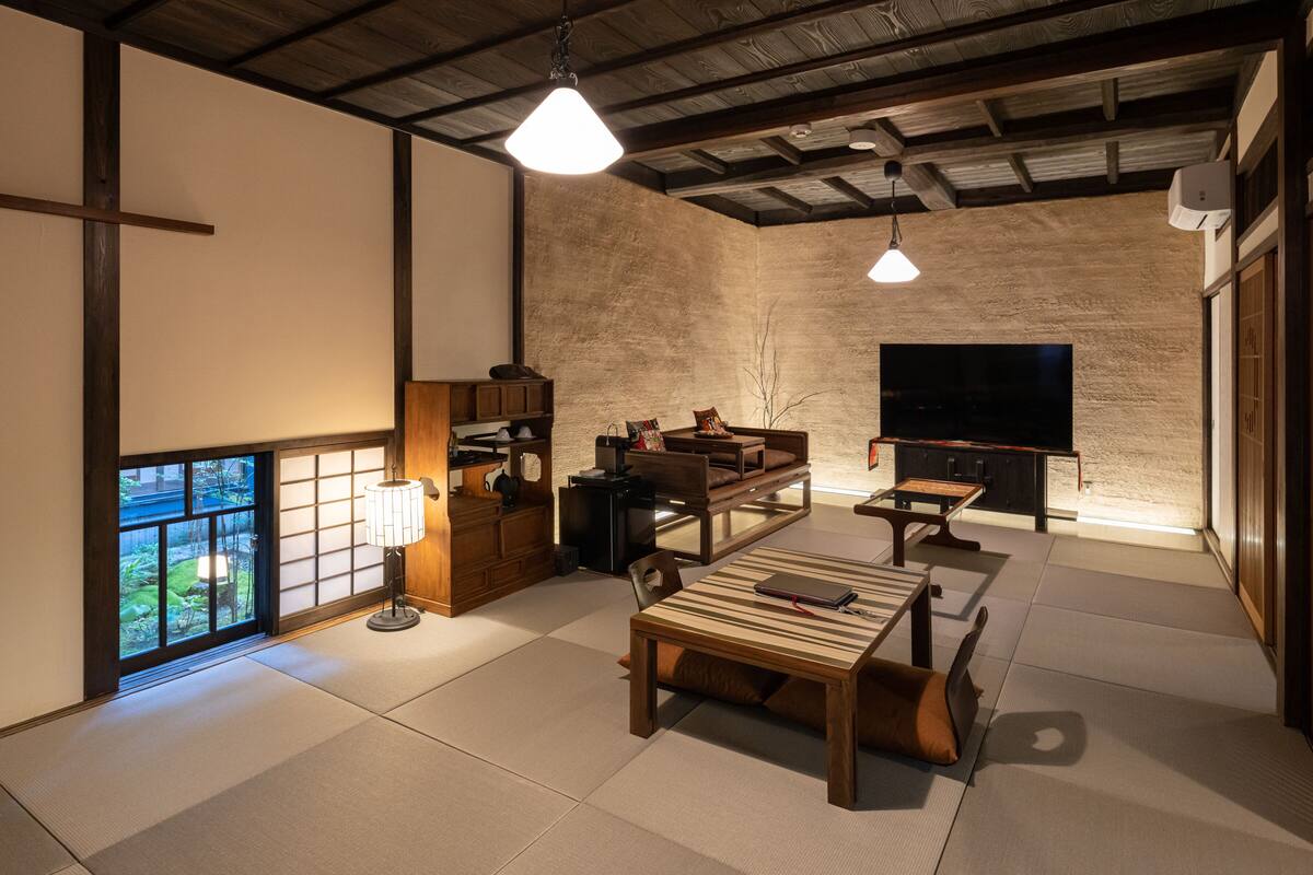 A traditional Japanese-style room with tatami flooring, a low table, a sofa, and a television.