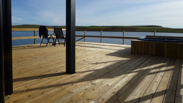 Une terrasse en bois avec un jacuzzi et des chaises, donnant sur un lac.
