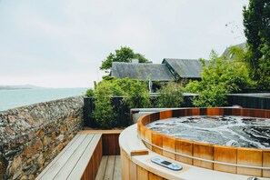 Ein Whirlpool auf einer Holzterrasse mit einer Steinmauer und Blick auf das Meer.