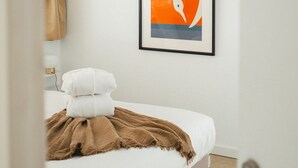 A bedroom with a bed, a framed abstract painting, and a door. - A boat house on the beach (Paimpol)