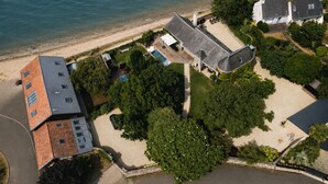 An aerial view of a coastal property with a swimming pool, a large tree, and a beach. - A boat house on the beach (Paimpol)