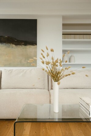 A living room with a glass coffee table, a beige sofa, a white vase with dried plants, and a painting on the wall. - A boat house on the beach (Paimpol)