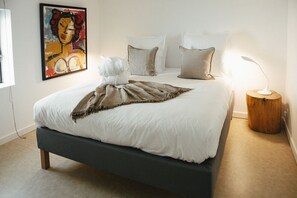 Ein ordentlich gemachtes Bett mit weißer Decke und brauner Tagesdecke, eine Nachttischlampe und ein Gemälde an der Wand.