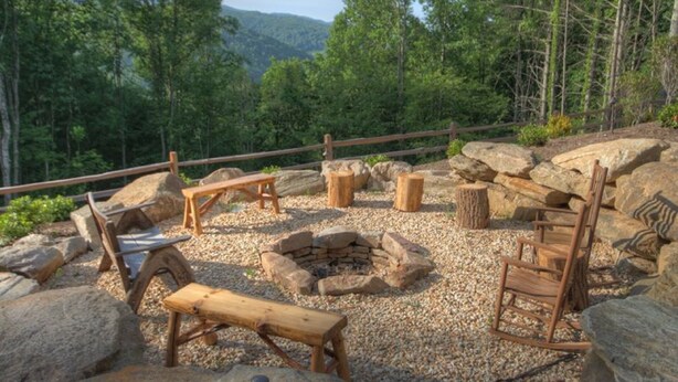 Un espace extérieur rustique aménagé avec des bancs en bois et un foyer entouré de rochers.