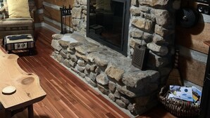 Un intérieur rustique avec une cheminée en pierre, des étagères en bois, une table en bois et un coin salon confortable.