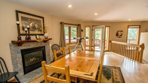 Une salle à manger avec une cheminée, une table en bois et des chaises. Un télescope sur trépied se trouve près des fenêtres.