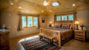 Une chambre dans une cabane en bois, avec un grand lit, deux tables de chevet, un banc et une fenêtre avec des rideaux.