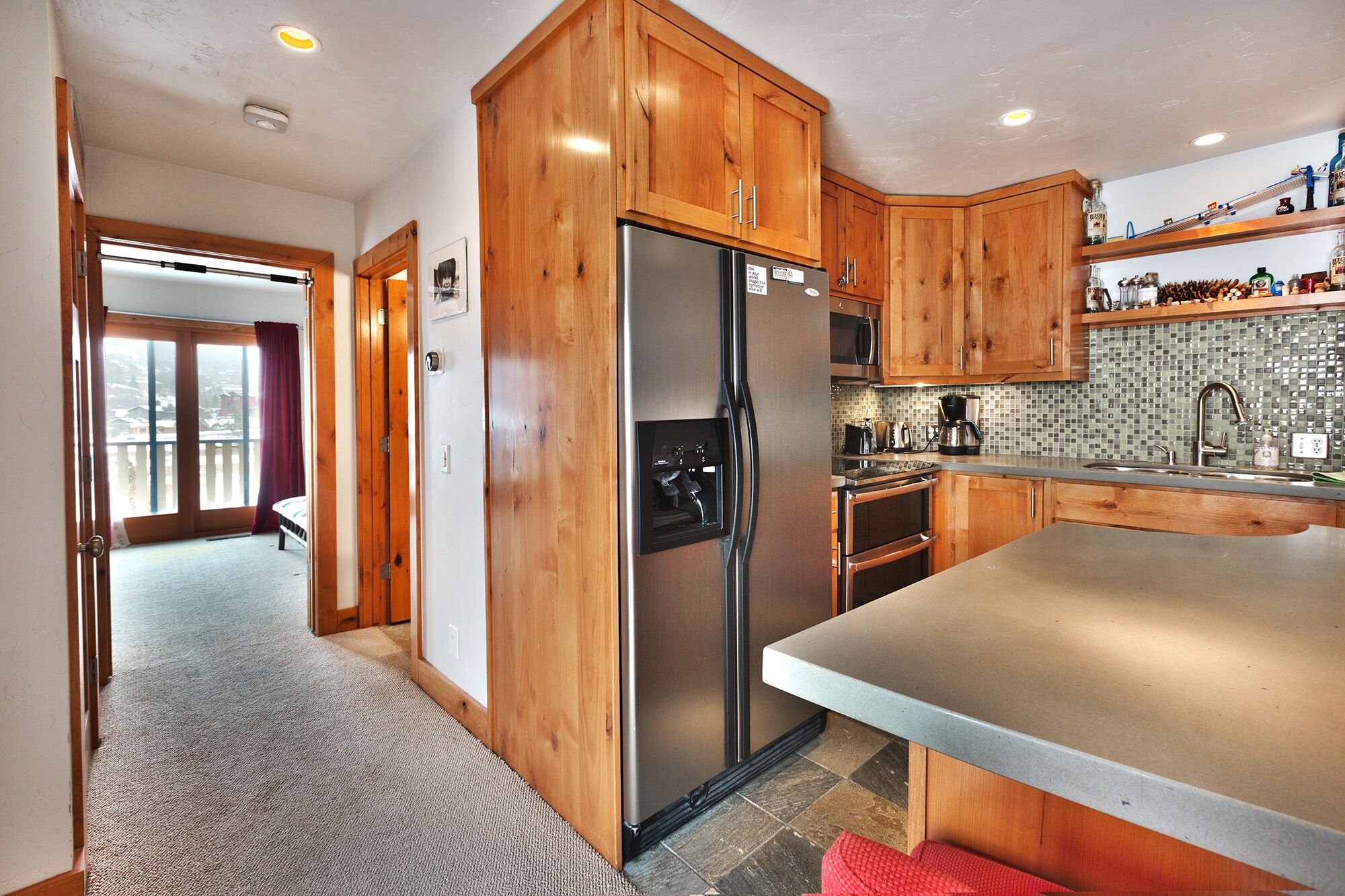 A modern kitchen with wooden cabinets, a stainless steel refrigerator, a microwave, and a tiled backsplash.