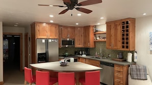 Eine moderne Küche mit Holzausstattung, einem Edelstahlkühlschrank, einer Mikrowelle und einem Deckenventilator.