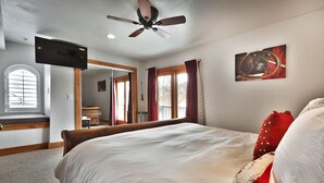 Ein Schlafzimmer mit einem Bett, einem Deckenventilator, einem Fernseher, einem Fenster mit Jalousien und einem Bild an der Wand.