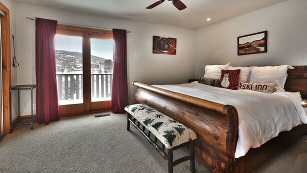 Ein Schlafzimmer mit einem Holzbett, einer Bank, einem Deckenventilator und einem Balkon mit Vorhängen.