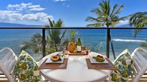 Un tavolo apparecchiato con una bottiglia di vino, ananas e frutta su un balcone che si affaccia sull'oceano e sulle palme.
