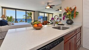 Una cucina moderna con una grande isola, una zona pranzo con vista sull'oceano e un soggiorno con divano e televisione.