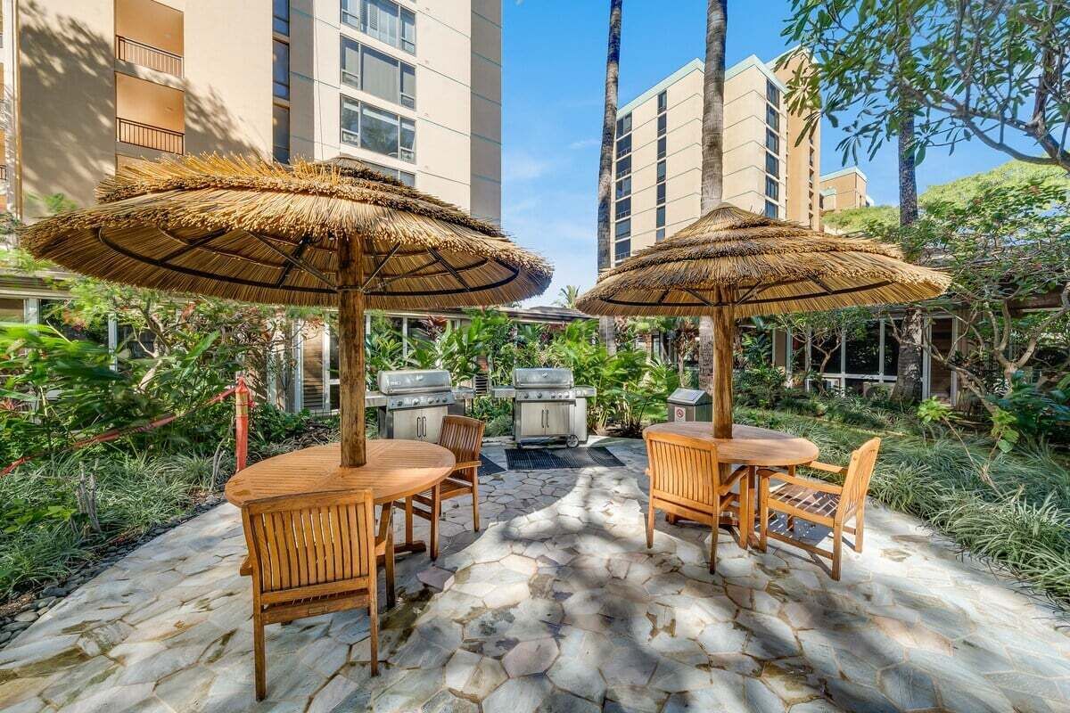 Un patio al aire libre con piso de piedra, mobiliario de madera y sombrillas de paja.