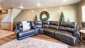 A sectional leather sofa in a living room with a wooden floor, a staircase, and a wreath on the wall.